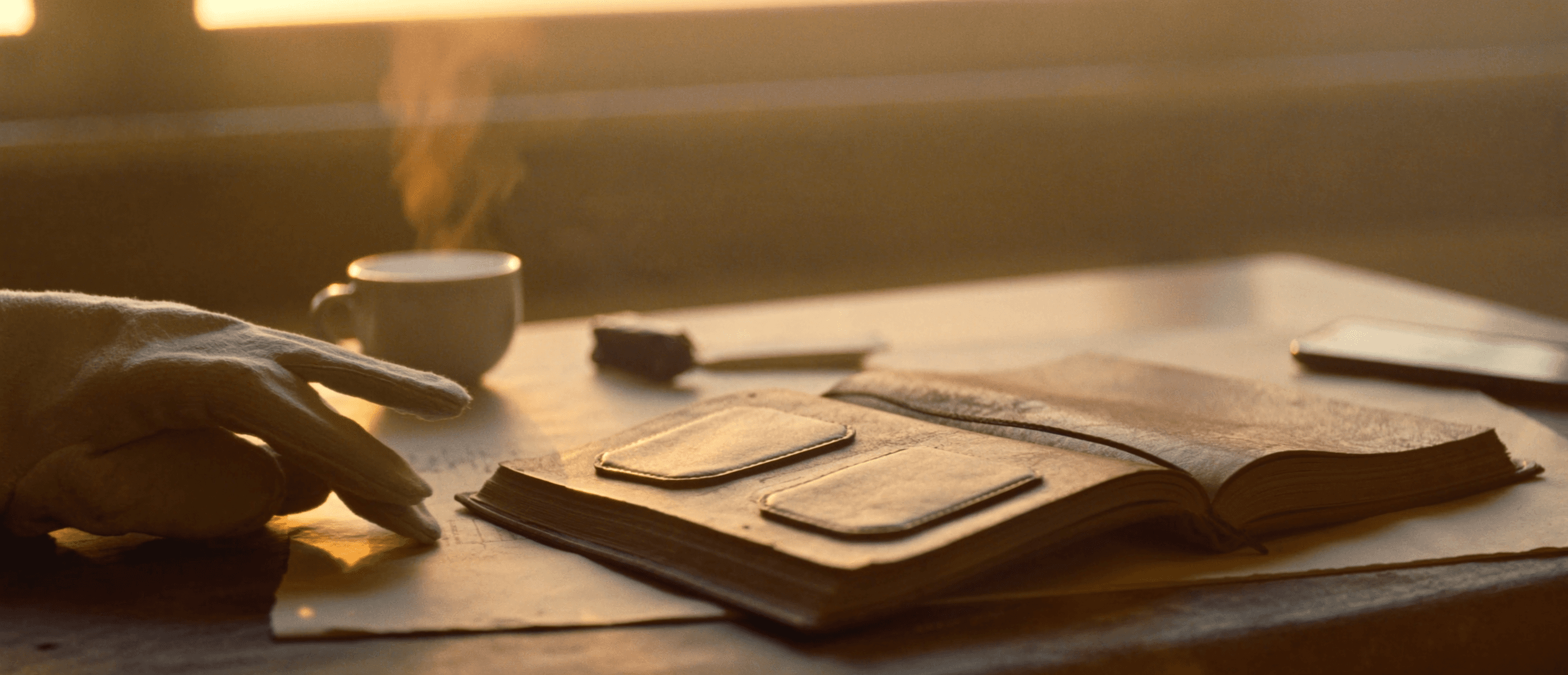 A tradesperson's desk at dawn: notebook, coffee, phone, gloves