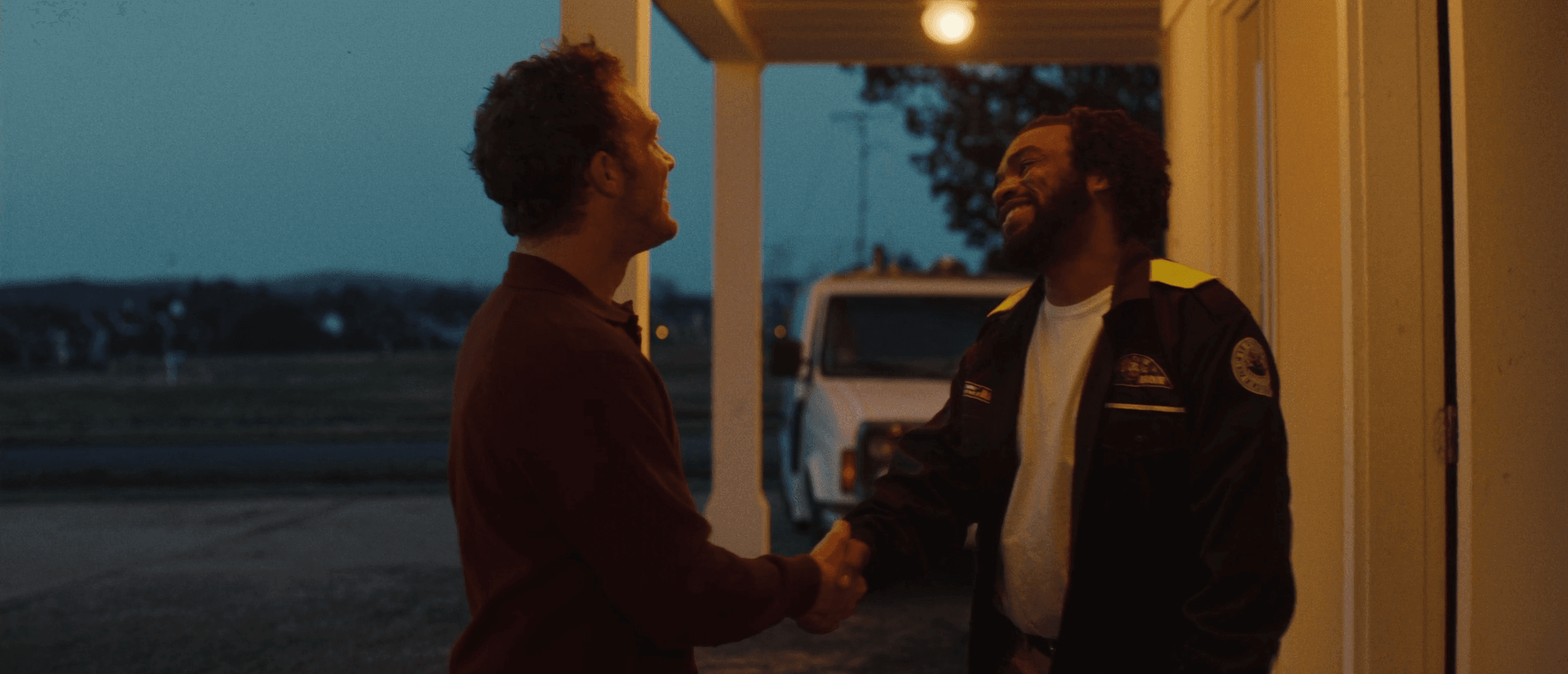 A tradesperson and homeowner shaking hands on a porch at dusk
