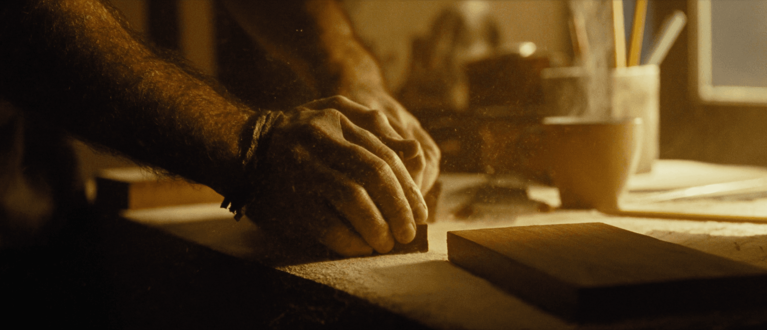 A craftsman's hands sanding oak in warm window light