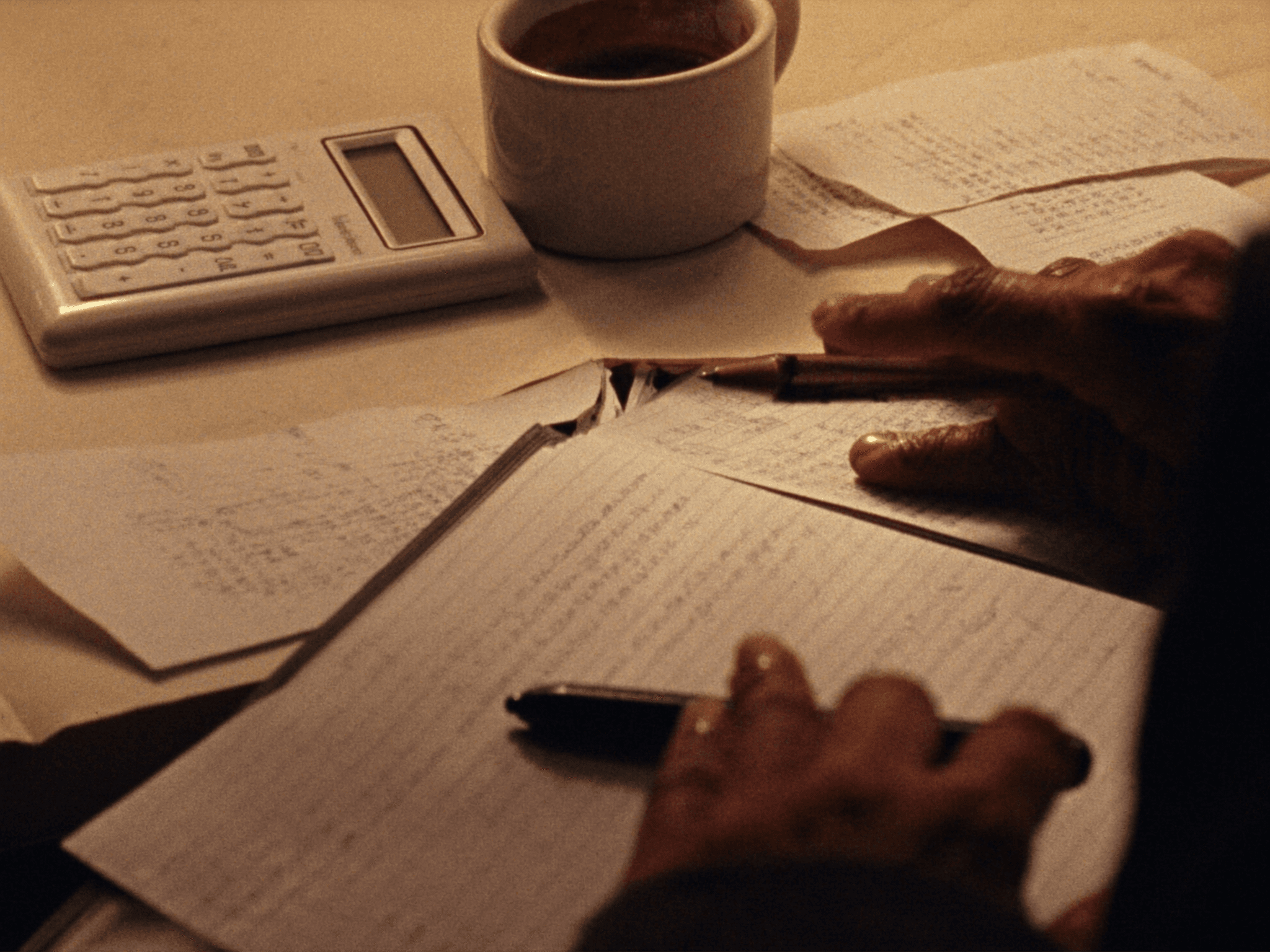 Hands over an open ledger with calculator and coffee